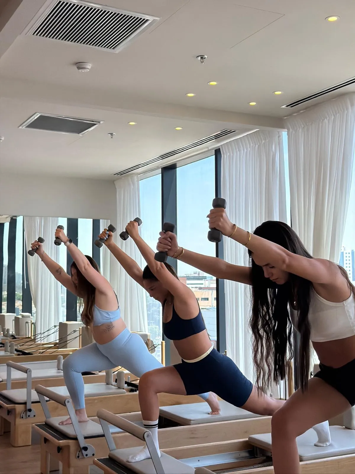 שלוש מתאמנות בתרגיל עם משקולות על מיטות רפורמר